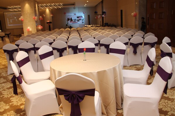 A conference room with rows of white chairs with purple sashes, a round table with a white tablecloth, and a projector screen in the background.