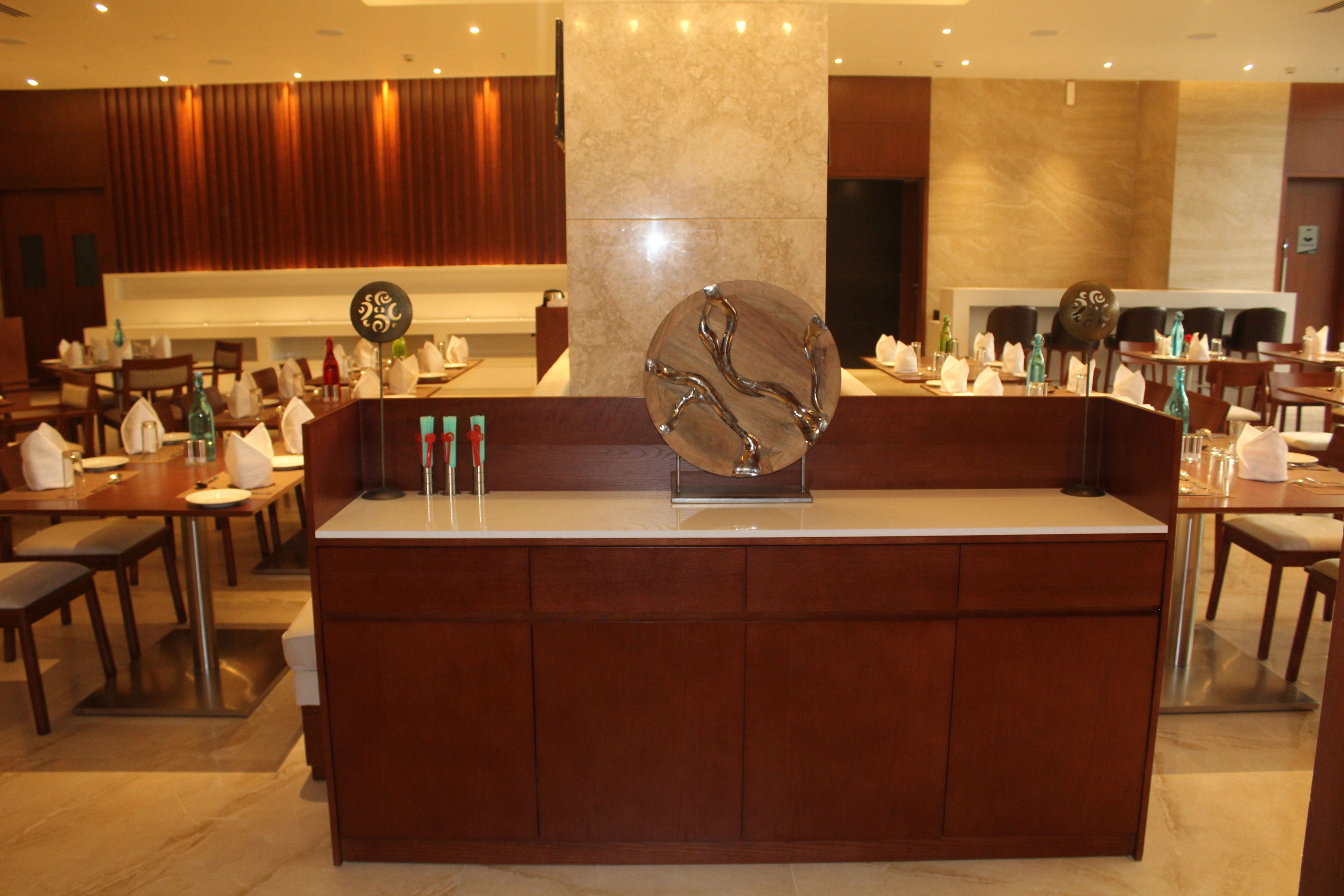 Vestíbulo de hotel con un mostrador de recepción central, varias mesas de comedor y una gran escultura decorativa.