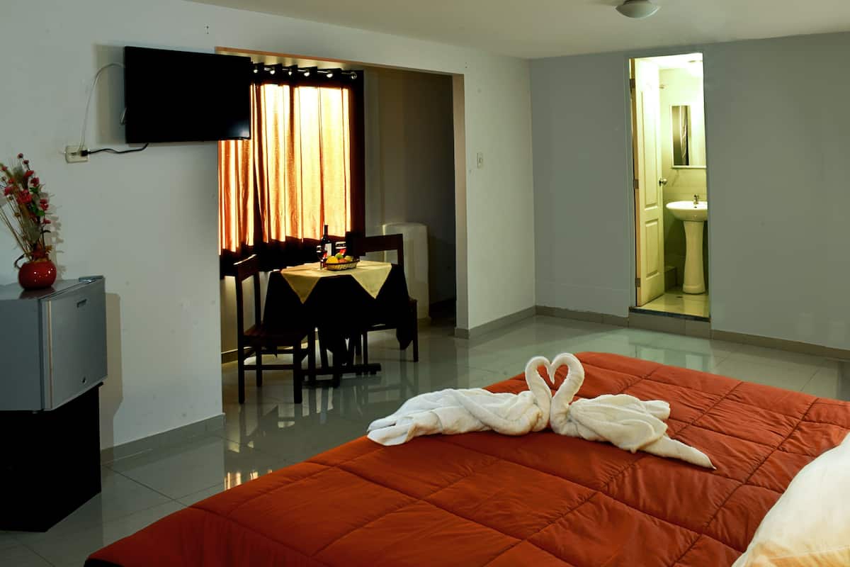 A hotel room with a bed, a TV, a dining area, and a bathroom.