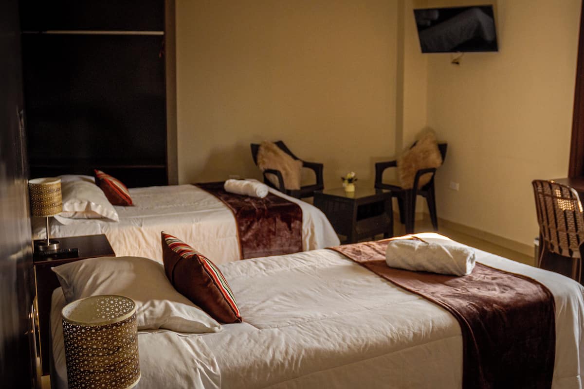 A hotel room with two beds, a desk, a chair, a TV, and a window with curtains.