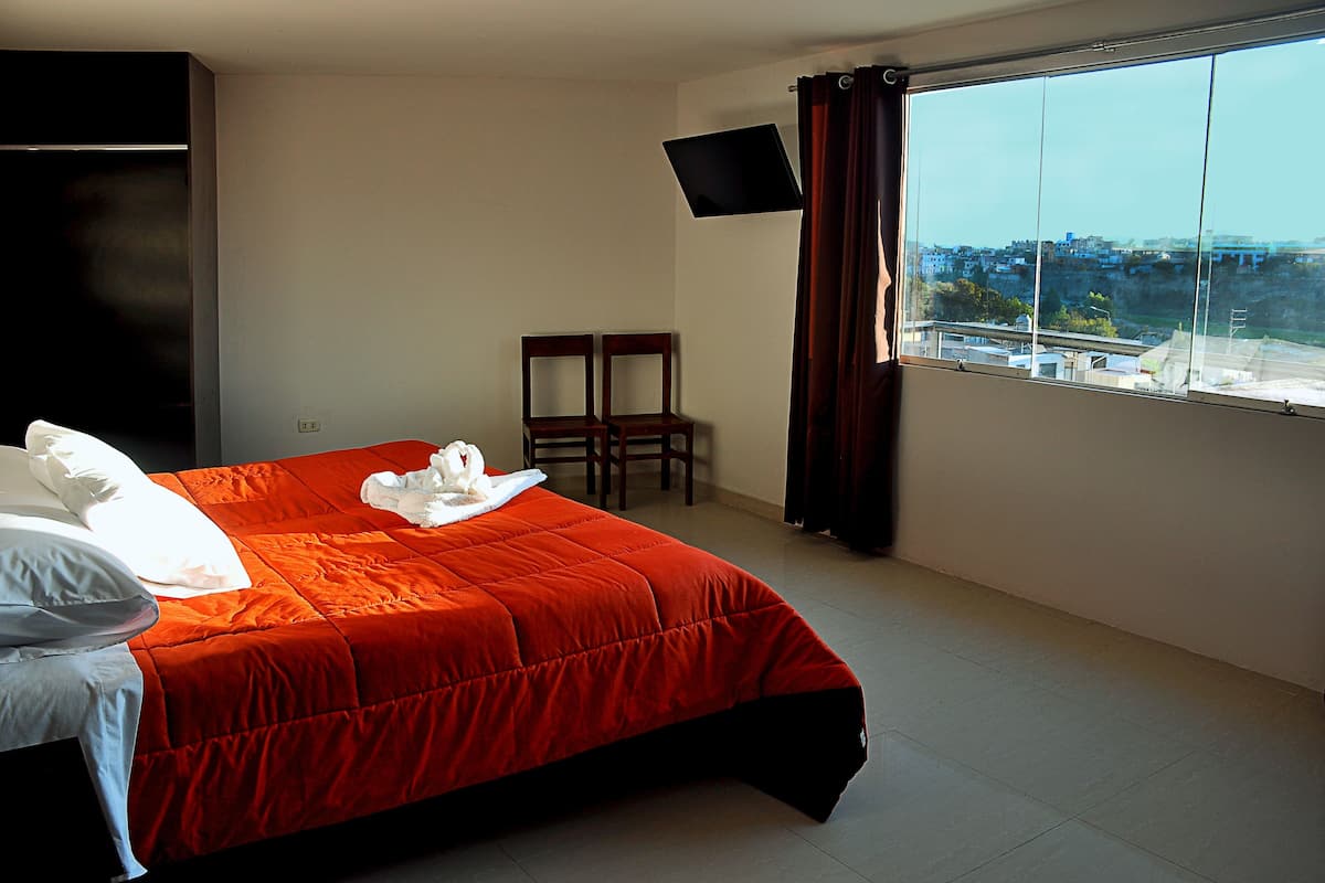 A hotel room with a bed, a TV mounted on the wall, and a window with a view of buildings.