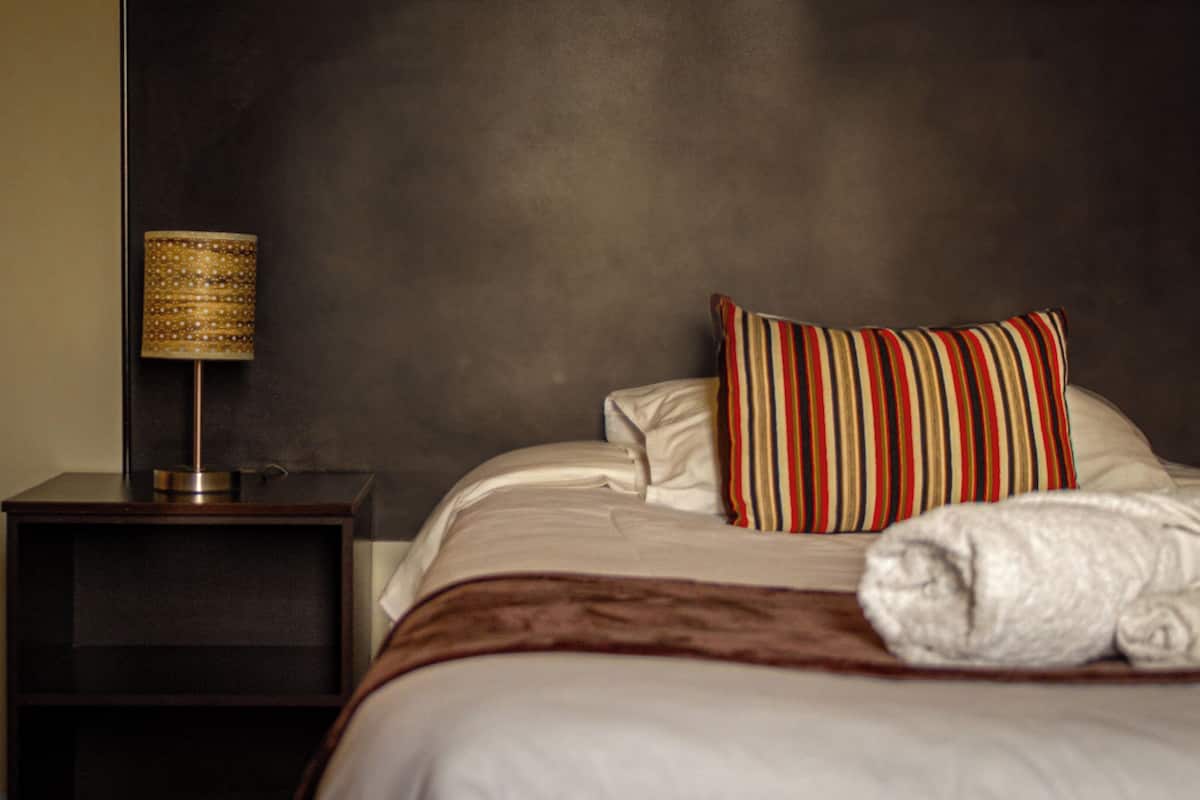 A neatly made bed with a striped pillow and a rolled towel, a bedside lamp, and a dark nightstand in a hotel room.