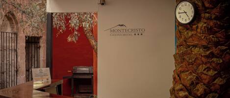 A reception desk with a clock, a sign for Montecristo Casona Hotel, and a stone wall.