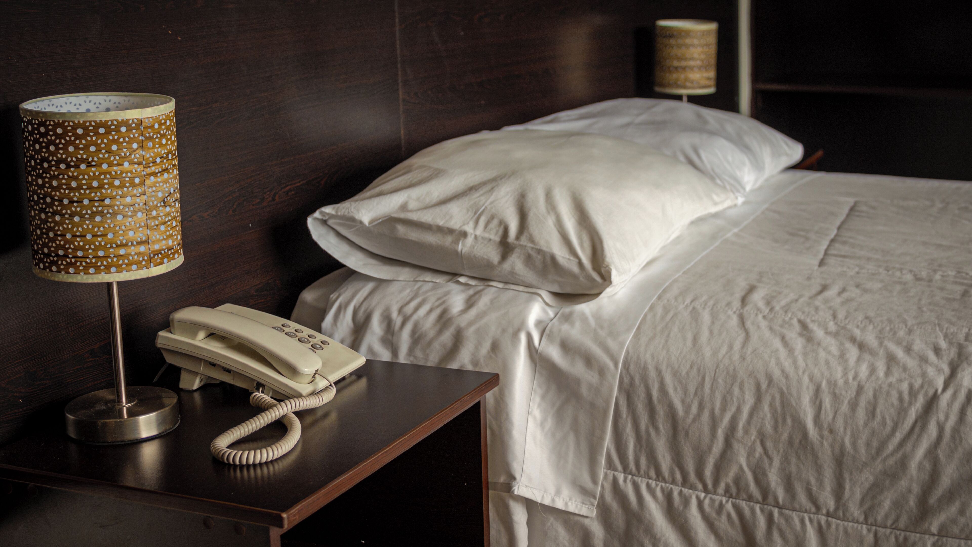 Una habitación de hotel con una cama, una mesita de noche con lámpara y teléfono, y otra mesita con lámpara.