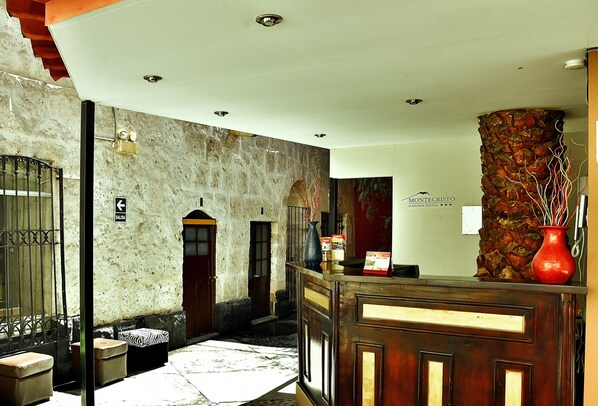 A hotel lobby with a reception desk, a stone wall, and a sign indicating the entrance. - MonteCristoHotel (Arequipa)