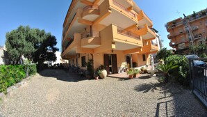 Un edificio a più piani con balconi, un cortile sterrato e piante in vaso.