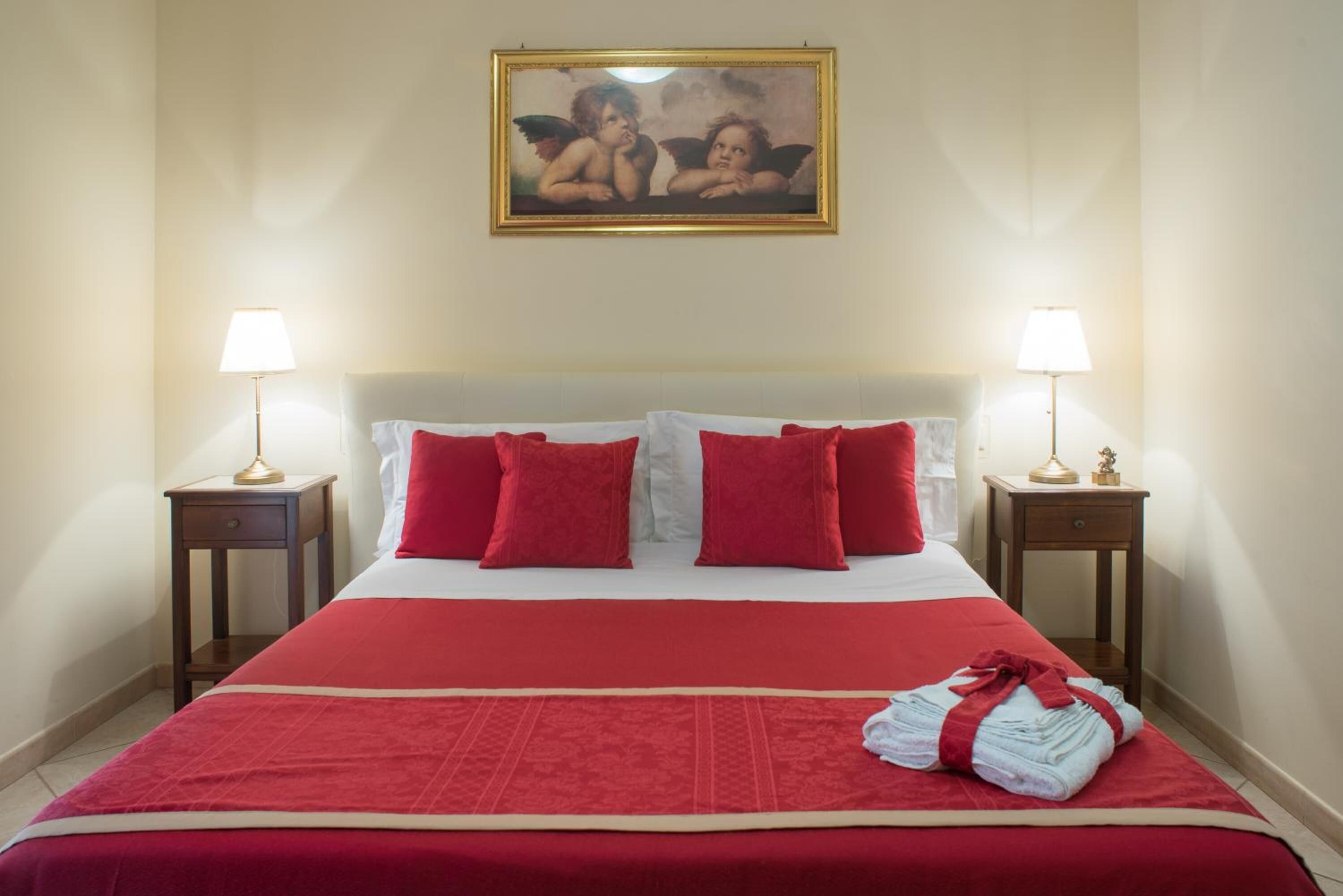 Camera d'albergo con un letto grande, biancheria rossa, due comodini con lampade e un quadro sopra il letto.