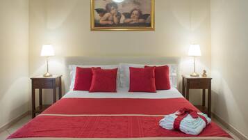 Camera d'albergo con un letto grande, biancheria rossa, due comodini con lampade e un quadro sopra il letto.