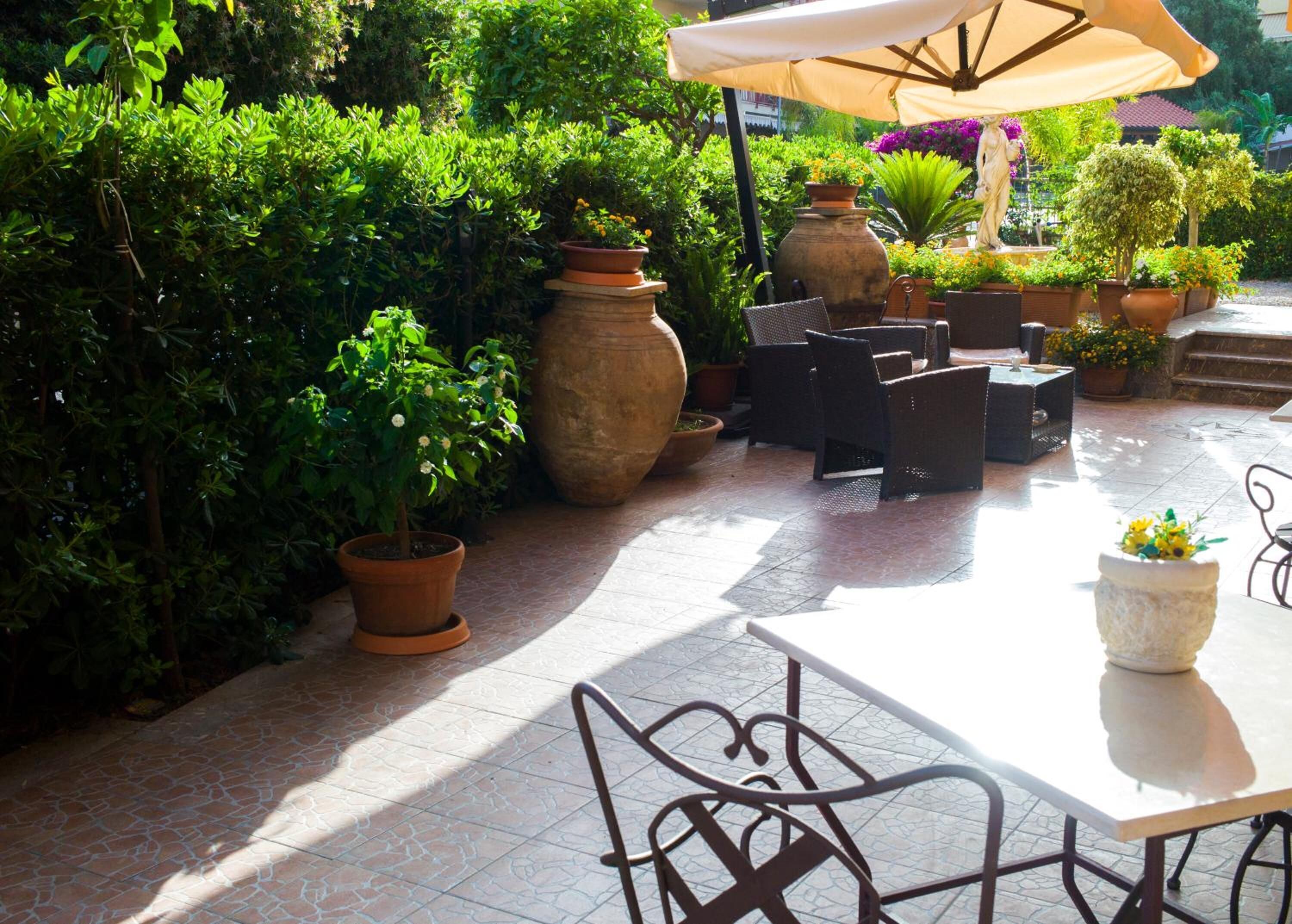 An outdoor patio area with a table and chairs, surrounded by potted plants and a statue.