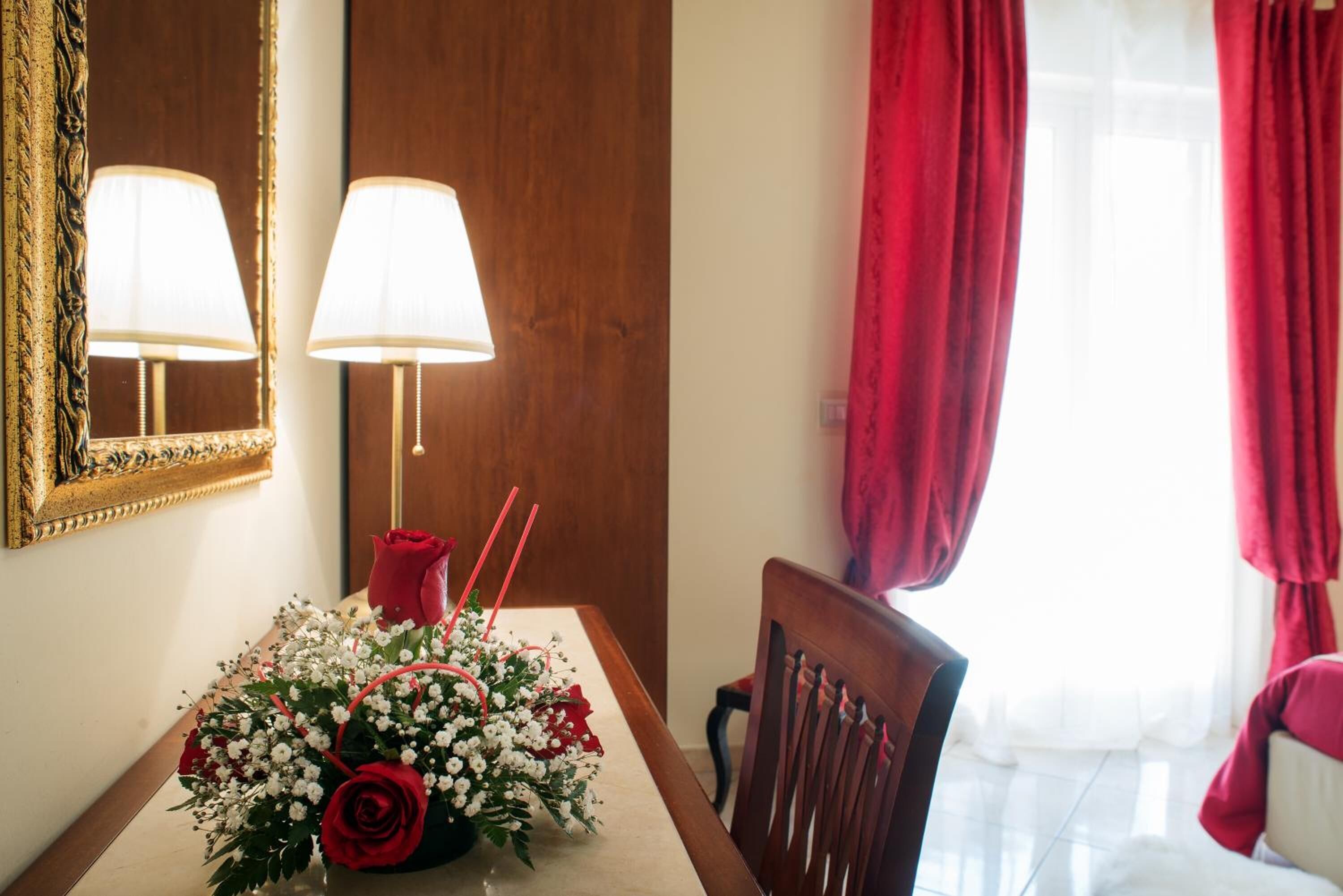 Un comedor con una mesa dispuesta para dos personas, una rosa roja y un ramo de flores.