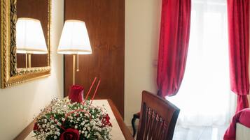 Un comedor con una mesa dispuesta para dos personas, una rosa roja y un ramo de flores.