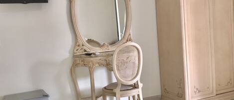 A room with a vanity, a mirror, a wardrobe, and a bed with towels.