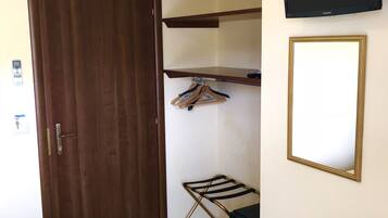 A hotel room with a bed, an air conditioning unit, a TV, a wooden door, a coat rack, and a small table.