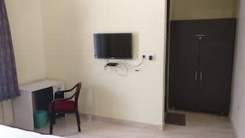 A room with a TV mounted on the wall, a desk with a chair, and a wardrobe.