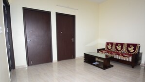 Una habitación con dos puertas de madera oscura, una mesa de centro con superficie de vidrio y un sofá con un cojín estampado.