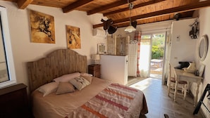 Een slaapkamer met een houten hoofdbord, een bed met een gestreept deken, een nachtkastje met een lamp, en een badkamer zichtbaar door een geopende deur.