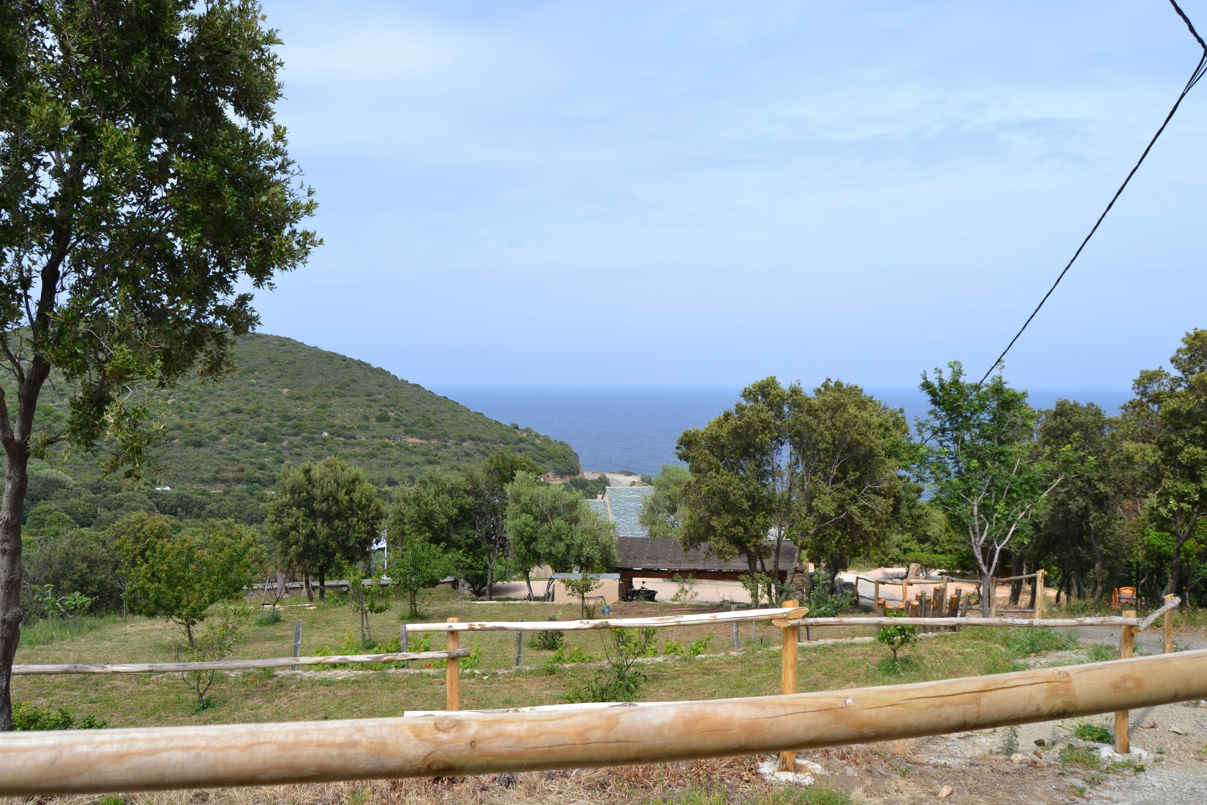 Un paisaje rural con vista al mar, una valla de madera y edificios dispersos.