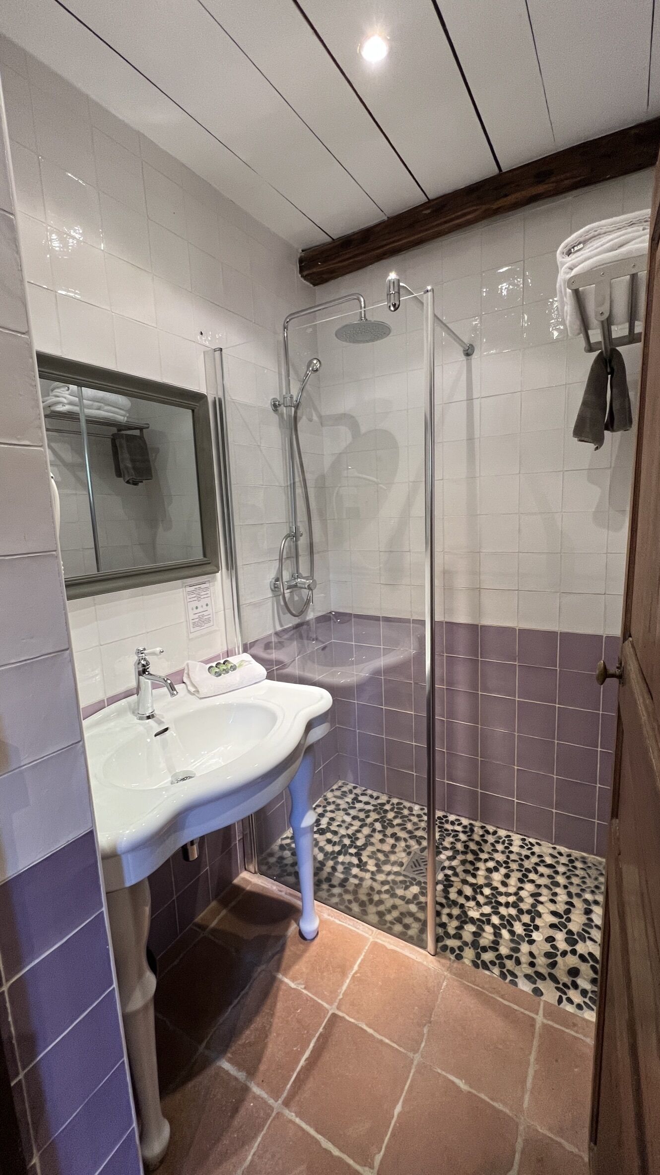 A bathroom with a white sink, a mirror, a shower with a glass door, and a tiled floor with a pebble pattern.