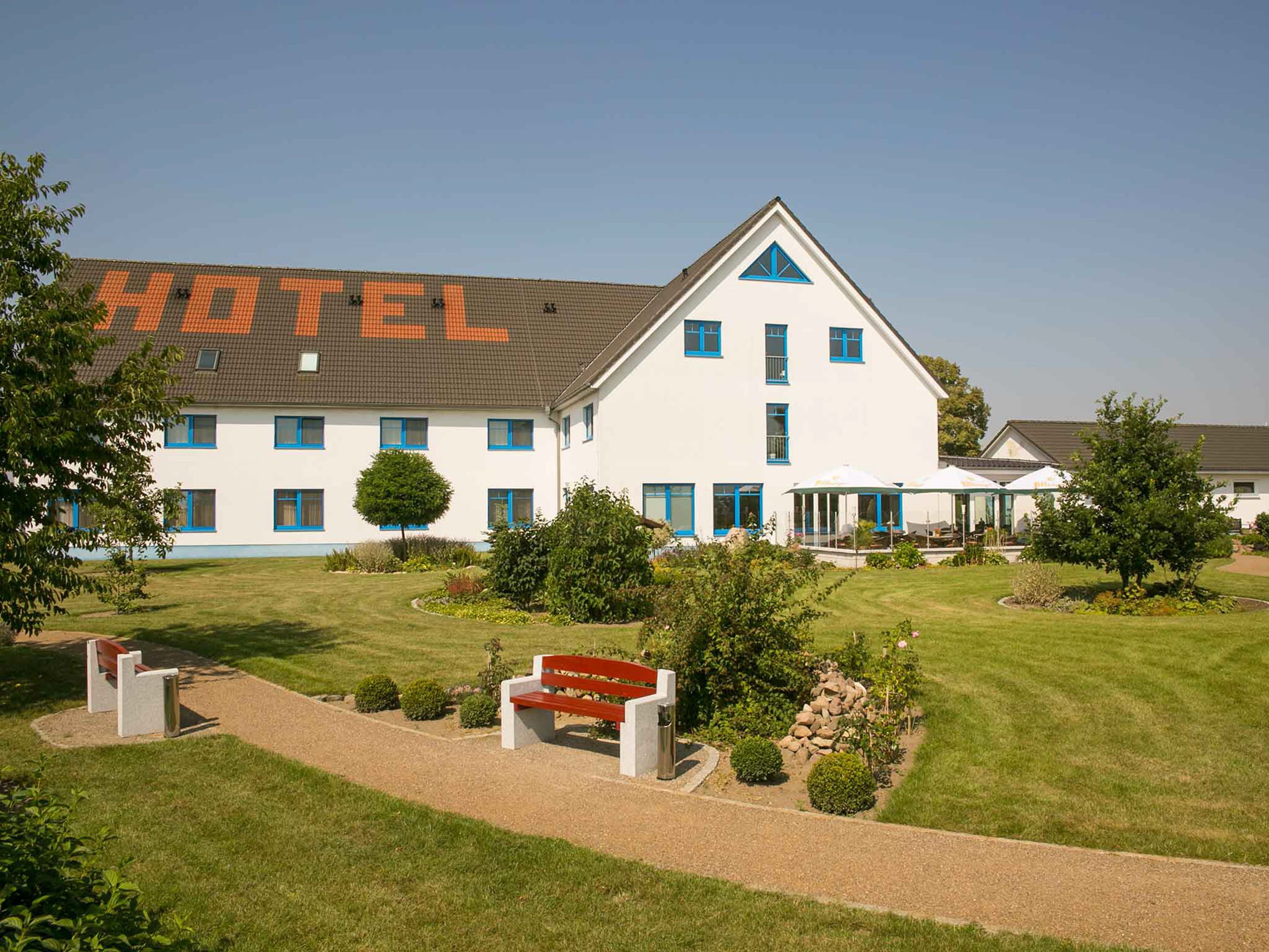 Un hotel con un cartel grande que dice "HOTEL" en primer plano, un césped cuidado y un edificio con varias ventanas y techo triangular.