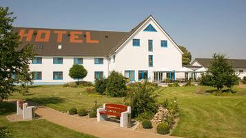 Un hotel con un cartel grande que dice "HOTEL" en primer plano, un césped cuidado y un edificio con varias ventanas y techo triangular.