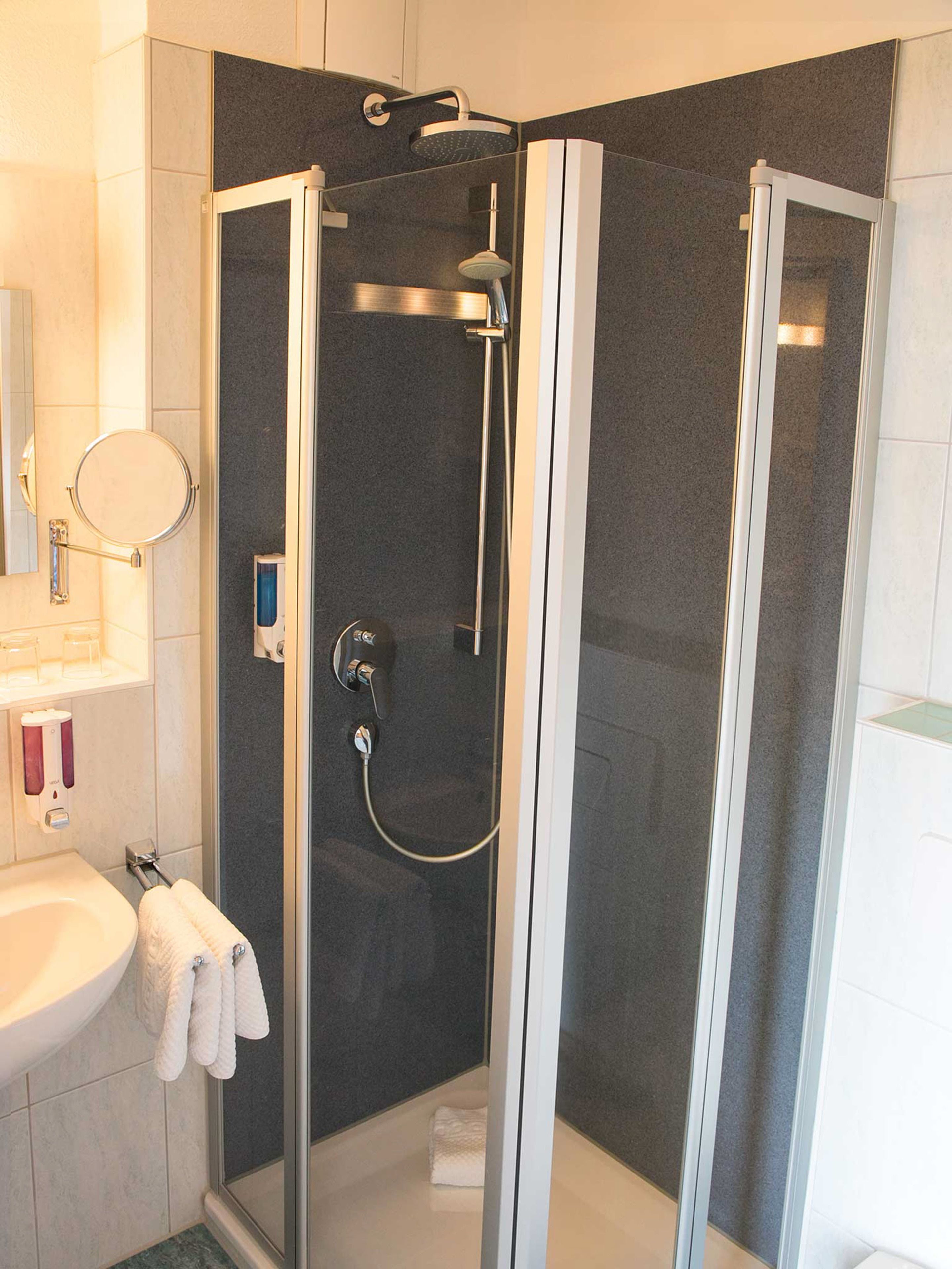 A modern bathroom with a glass-enclosed shower, a white sink, and a towel rack.