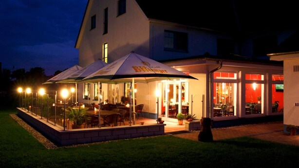 A building with a covered outdoor seating area, glass doors, and a well-lit interior. - Hotel Pommernland (Anklam)