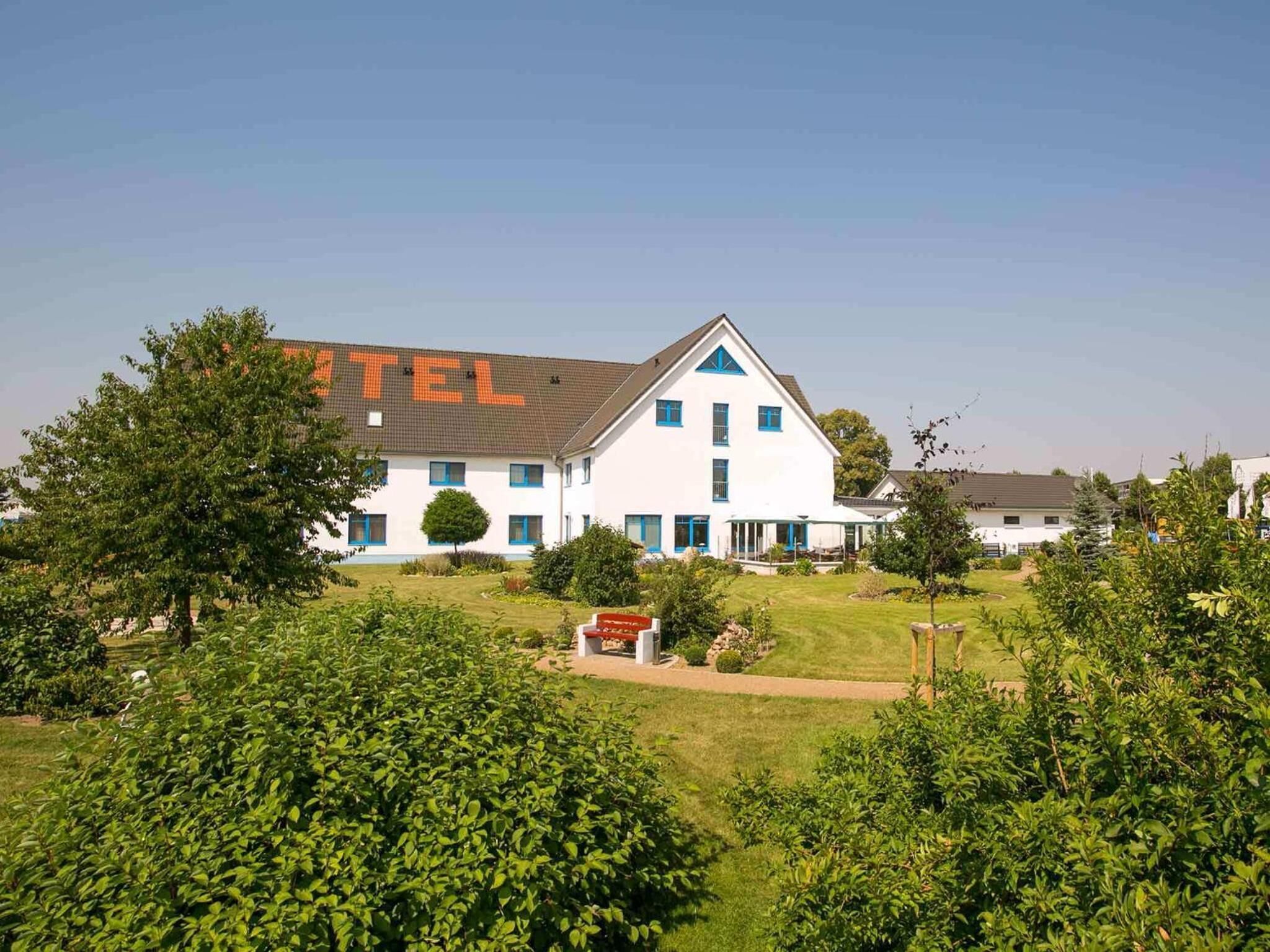 A white building with blue accents, labeled "HOTEL" on the side, surrounded by greenery.