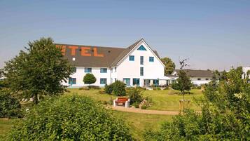 A white building with blue accents, labeled "HOTEL" on the side, surrounded by greenery.