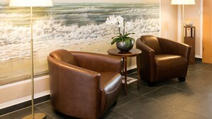 A room with a large ocean mural, two leather armchairs, a small table with a vase of flowers, and two floor lamps. - Hotel Pommernland (Anklam)