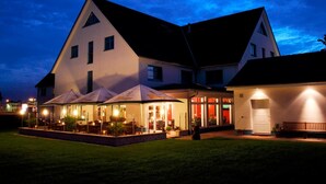 A large, two-story building with a prominent triangular roof and a well-lit outdoor patio area. - Hotel Pommernland (Anklam)