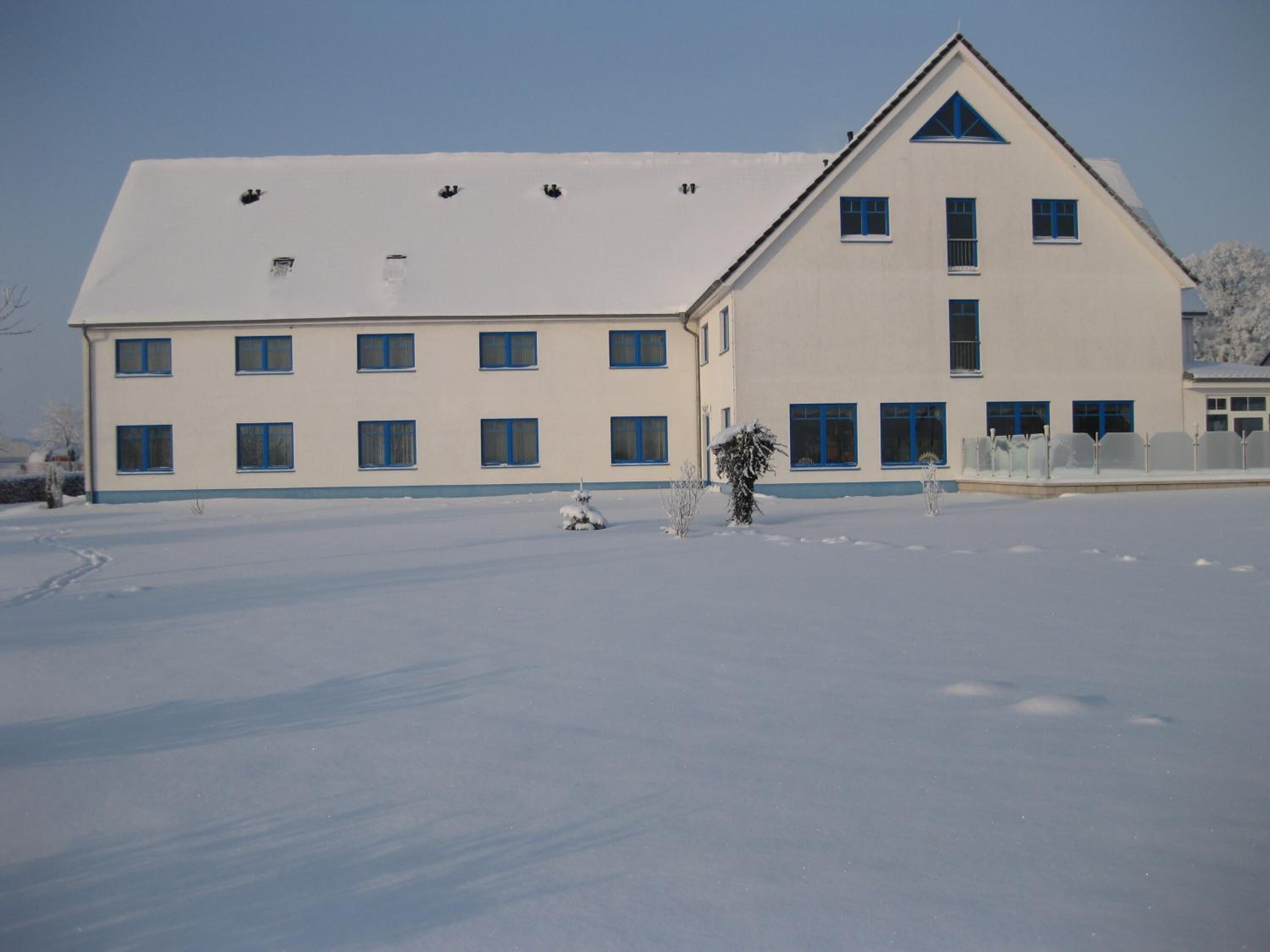 A large, multi-story building with a symmetrical facade, multiple windows, and a snow-covered ground.