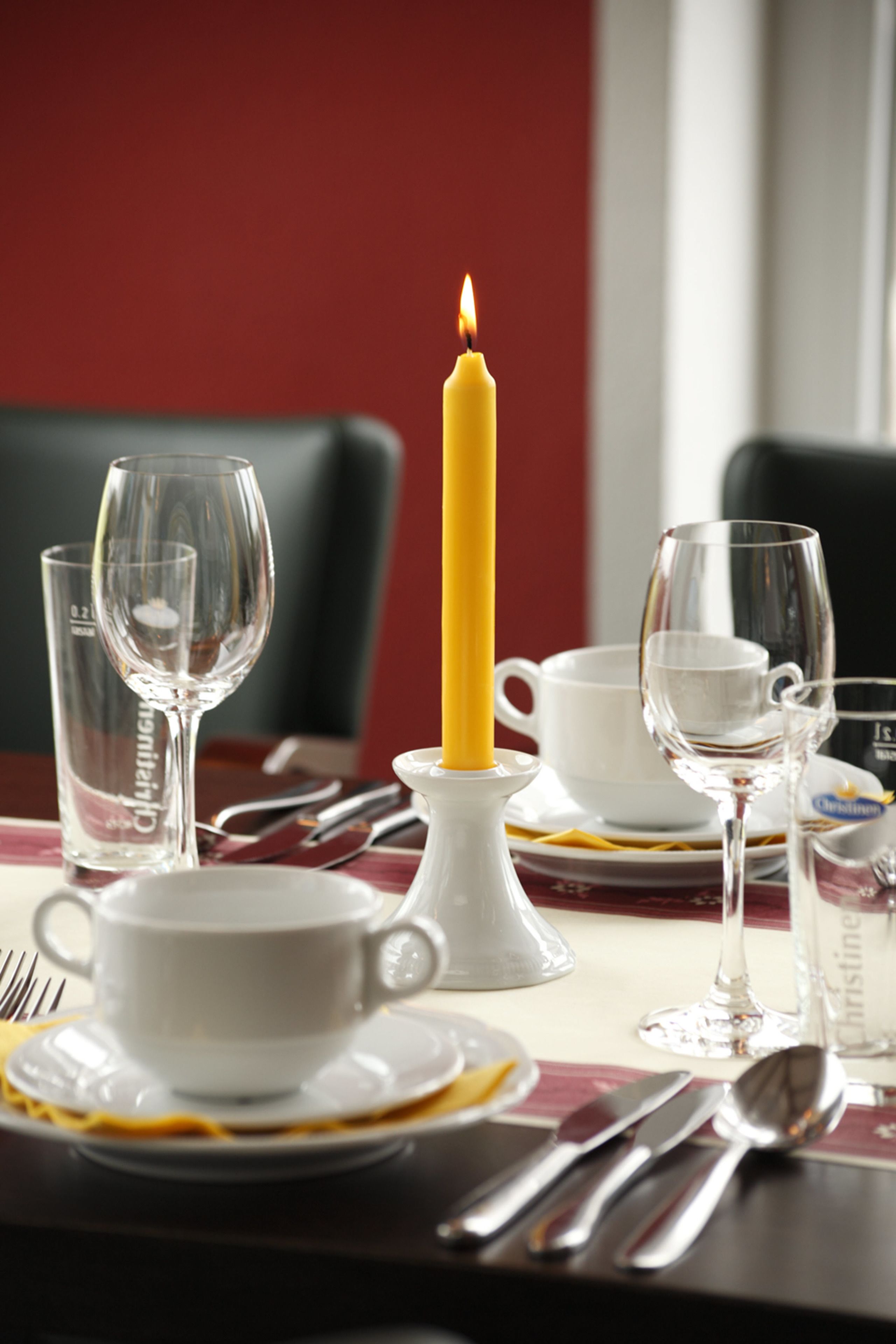 A dining table set with white plates, cutlery, and clear glassware. A lit yellow candle is placed in the center.
