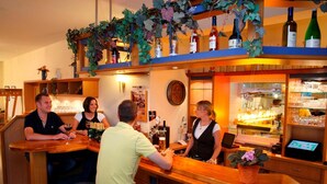 A bar area with wooden furniture, a bartender, and shelves with bottles. - Hotel Pommernland (Anklam)