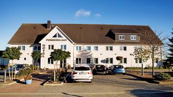 Um hotel com design moderno, destacando uma placa grande com a inscrição 'POMMERLAND', um acesso pavimentado e vários carros estacionados.