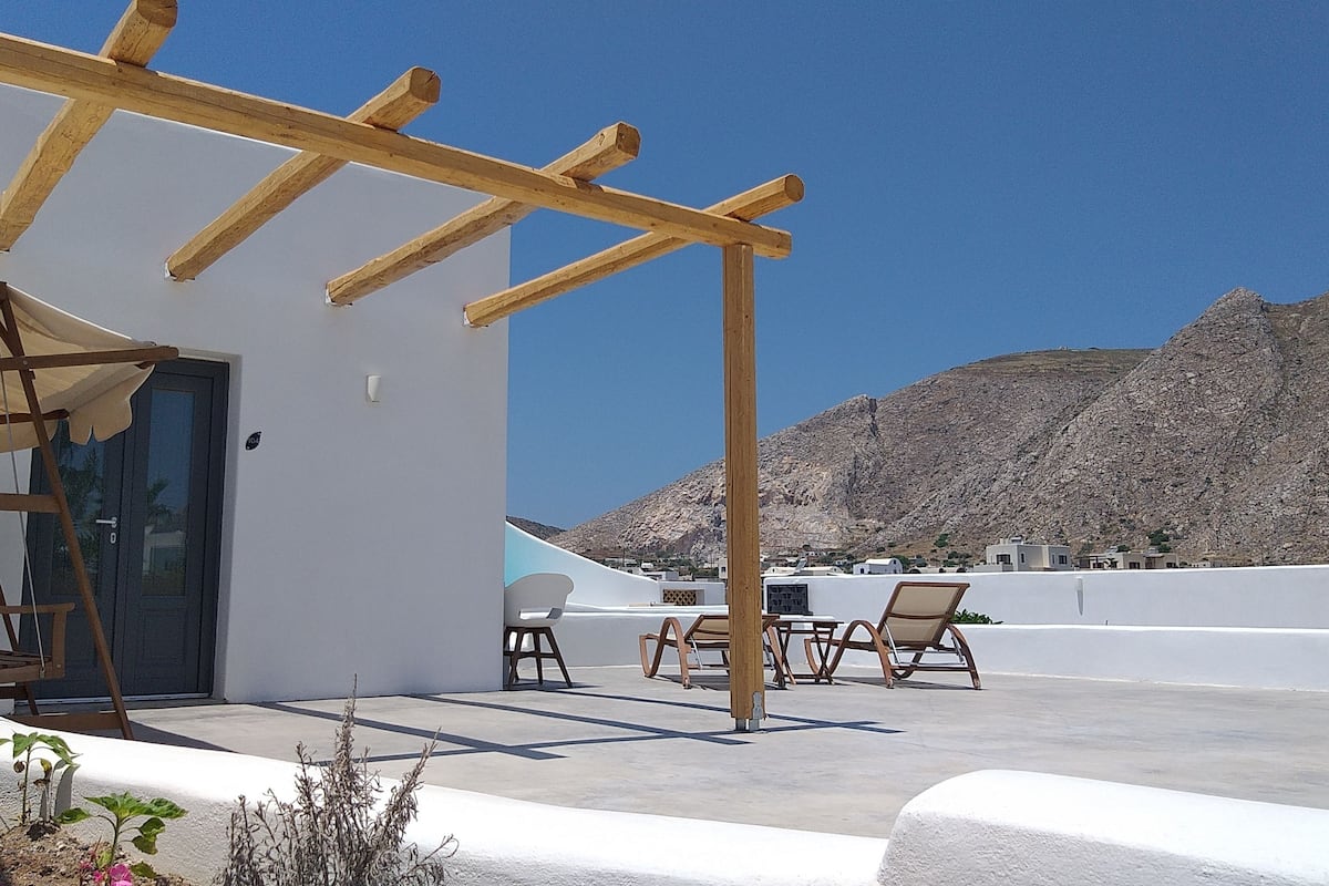 Terraza en la azotea con pérgola, mobiliario exterior y montañas al fondo.