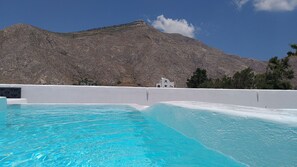 Uma piscina com água azul cristalina, um edifício branco e uma montanha ao fundo.