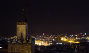 Vista nocturna de un paisaje urbano con una torre destacada y una zona iluminada en primer plano.