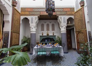 Un interior tradicional marroquí con suelo a cuadros, arcos ornamentados y una mesa preparada para el desayuno.