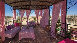 A covered outdoor seating area with a table and chairs, surrounded by pink curtains, overlooking a cityscape. - Riad Sanaa Rose (Fes)