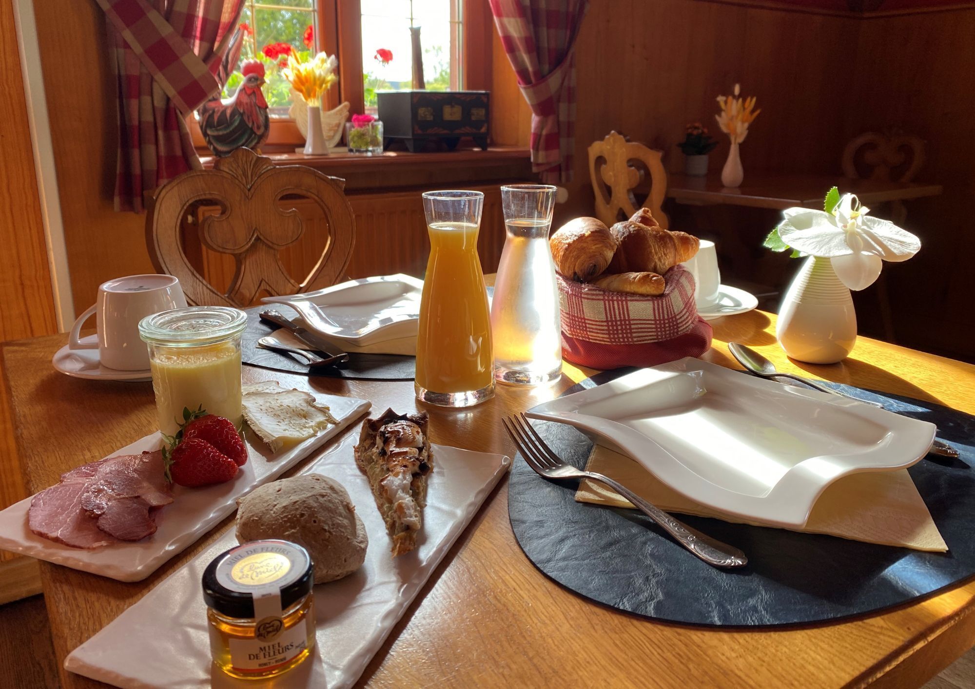A breakfast table with croissants, strawberries, ham, and a bottle of honey.