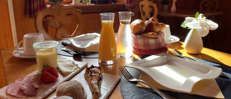 Een ontbijttafel met croissants, aardbeien, ham en een fles honing.