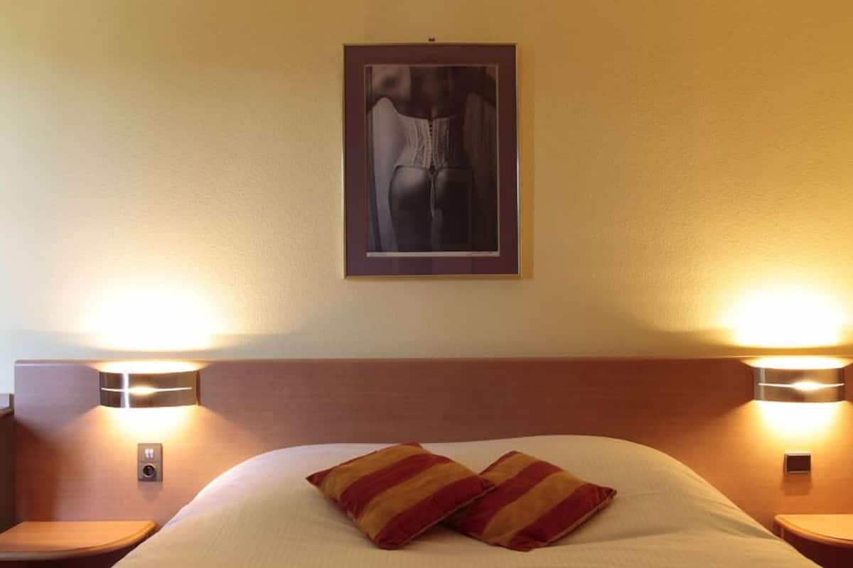 A hotel room with a bed, two bedside lamps, and a framed artwork on the wall.
