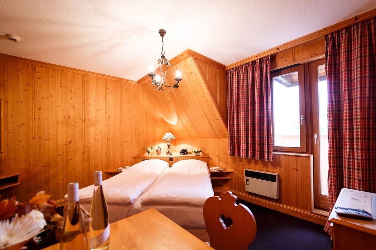 A cozy room with wooden walls, a bed with white linens, a chandelier, a table with a bottle, and a chair.