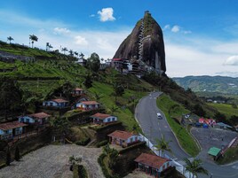 Un pueblo costero con una destacada formación rocosa, un camino serpenteante y pequeñas casas con techos rojos.