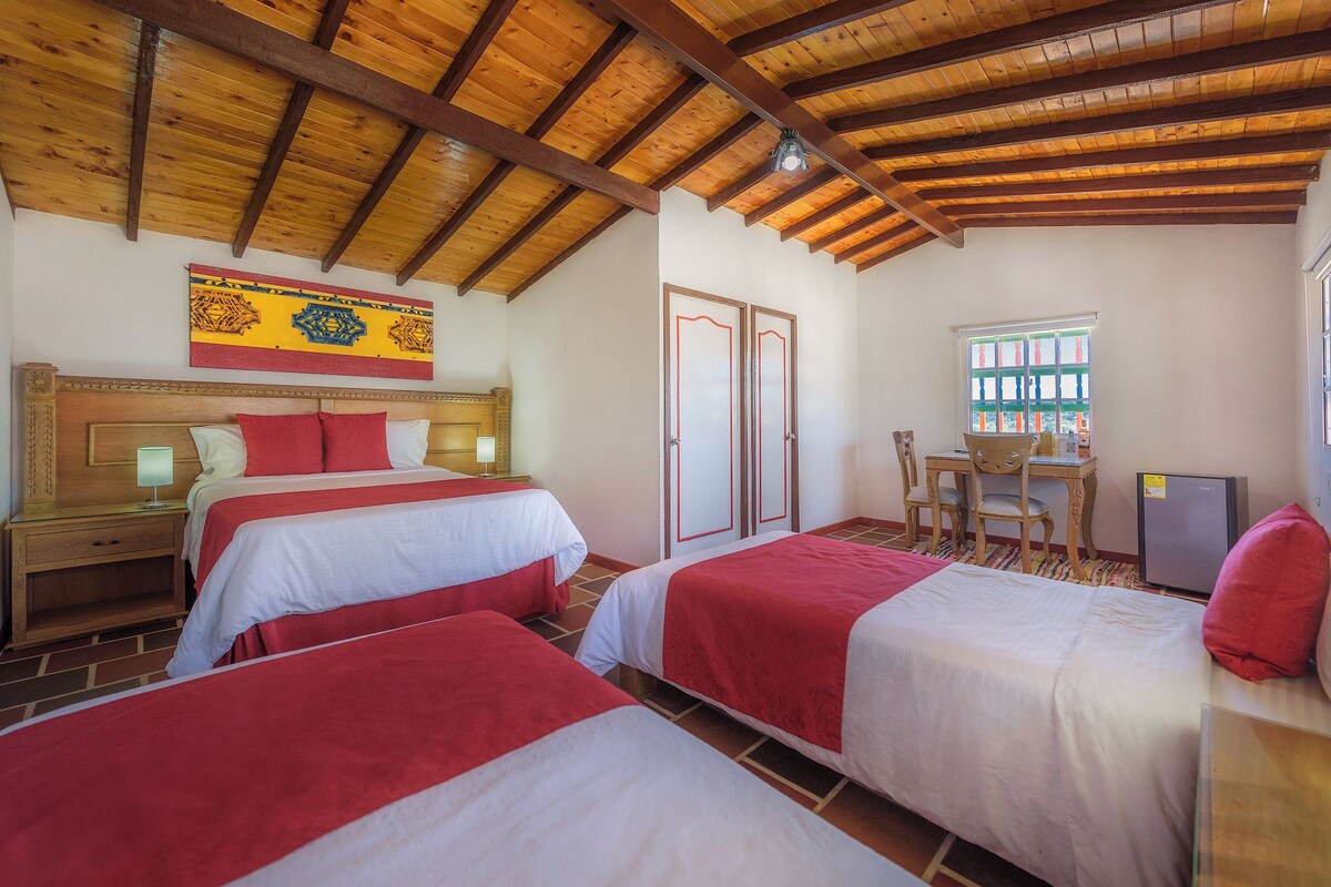 Une chambre d’hôtel avec deux lits, un plafond en bois, un bureau avec une chaise et une fenêtre.