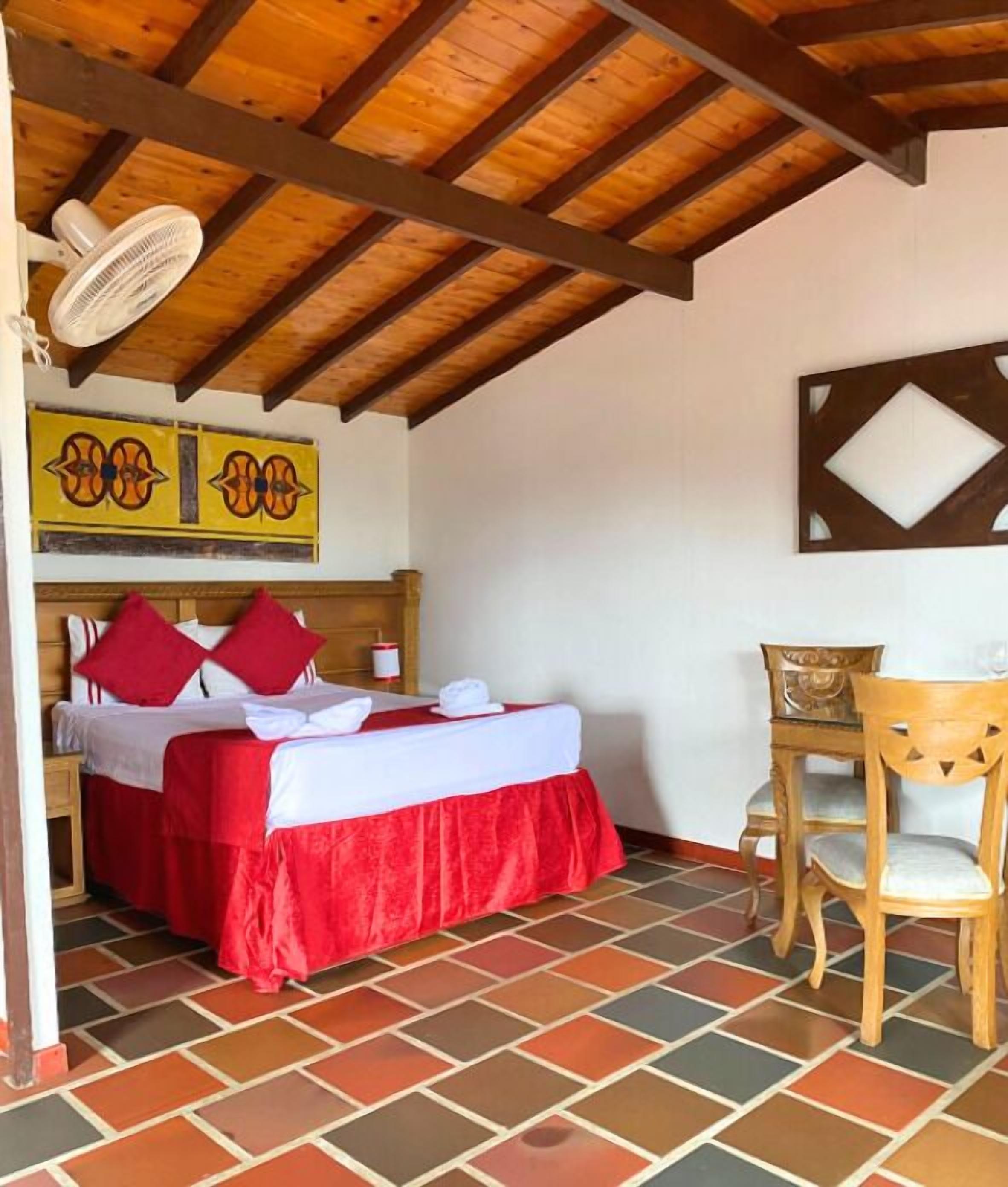 A room with a bed, a chair, a fan, and a wall with a decorative piece.