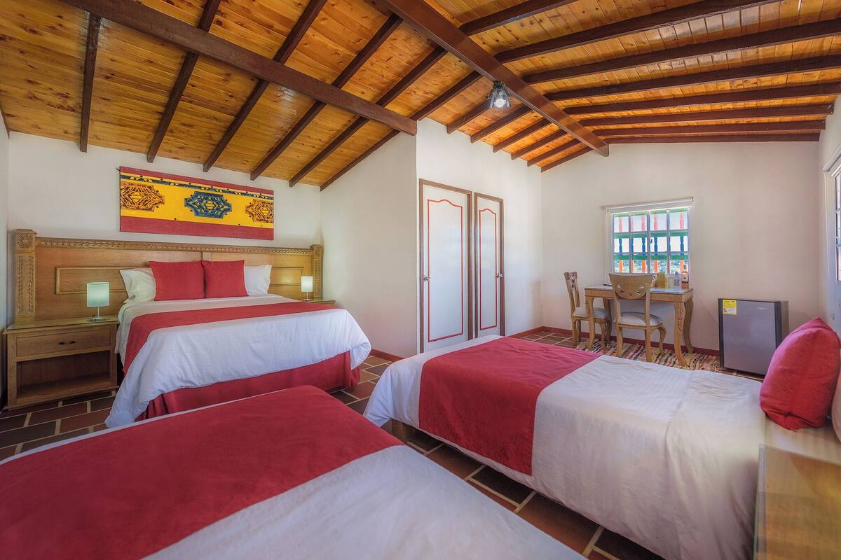 Une chambre d’hôtel avec deux lits, un plafond en bois, un bureau avec une chaise et une fenêtre.