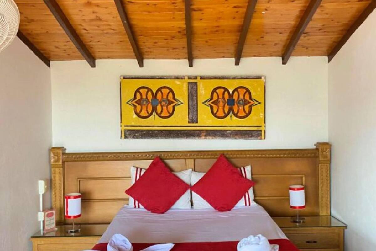 Une chambre d’hôtel avec un plafond en bois, un lit avec une literie rouge, deux oreillers rouges et un tableau au-dessus du lit.