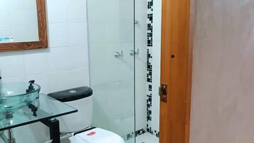 Un baño con lavamanos de vidrio, inodoro y zona de ducha.