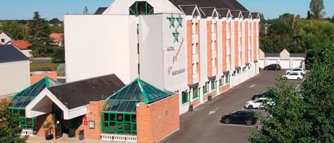 A hotel with a distinctive white facade and green accents, featuring a row of windows and a prominent logo.